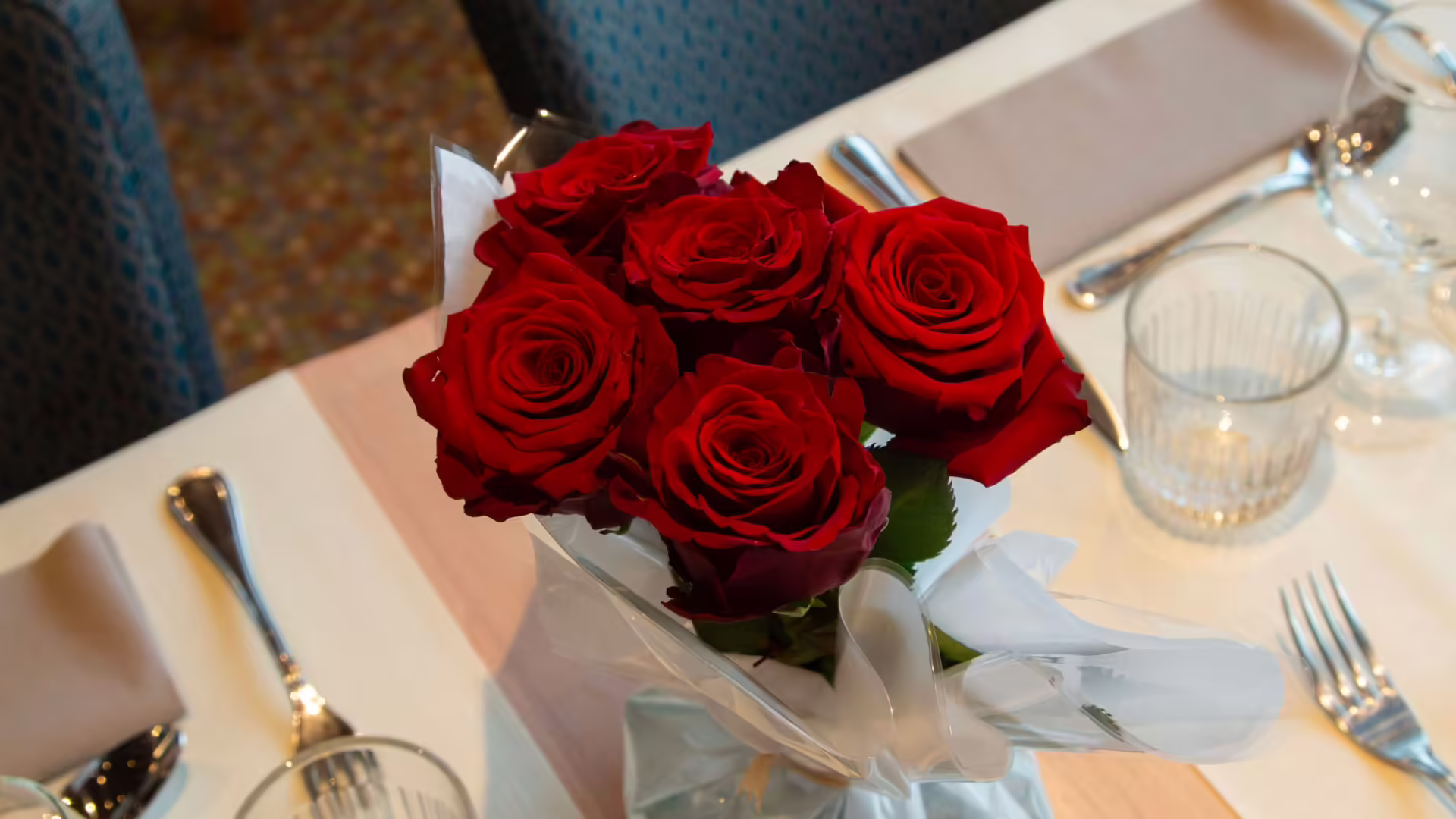 Table décorée avec un bouquet de roses rouges pour un dîner croisière romantique sur la Seine à Paris, offrant une vue sur un pont emblématique | Le Capitaine Fracasse